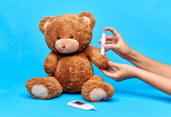 Wall Mural - medicine, healthcare and diabetes concept - hands with insulin pen making injection to teddy bear toy over blue background