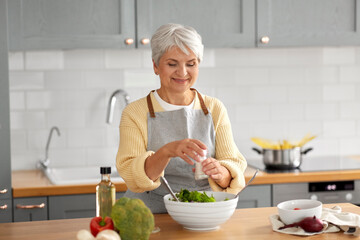 Wall Mural - healthy eating, food cooking and culinary concept - happy smiling senior woman with salt making vegetable salad on kitchen at home