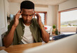 © Sarah - Exhausted Young adult black male massaging his temples while he works on laptop from home in modern kitchen.