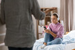 misbehavior, conflict and family concept - angry mother entering room and sad daughter in headphones with smartphone sitting on bed at home