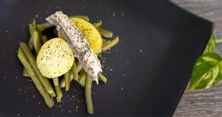 Wall Mural - Closeup shot of a dish of green beans with potatoes and tuna belly fillets on a dark plate