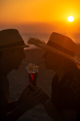 Wall Mural - A man and a woman are drinking a cocktail at sunset by the sea. Selective focus.