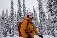 Carefree Female Skier In Goggles Looking Up At Snowy Trees