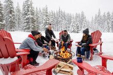 Family Warming Hands At Fire Pit At Snowy Winter Resort