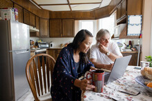 Senior Couple Drinking Coffee And Using Laptop At Kitchen Table