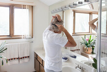 Senior Man Brushing Hair At Bathroom Mirror