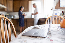 Couple Talking And Drinking Coffee Behind Laptop On Kitchen Table