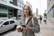 Portrait Of Woman Holding Phone And Hot Drink On Sidewalk