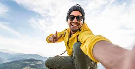 Wall Mural - Young hiker man taking selfie portrait on the top of mountain - Happy guy smiling at camera - Hiking and climbing cliff