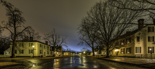 Sticker - Buildings in the illuminated wet street with leafless trees against a cloudy sky at night