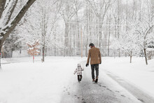 Dad And Toddler Walk Down Street On A Snowy Day In A Neighborhood