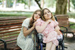 © sofiko14 - Portrait of two happy female friends looking at camera while spending free time at summer park. One woman sitting on wooden bench, another using wheelchair.