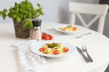 Wall Mural - Italian pasta with cherry tomatoes and garnished with a sprig of parsley. Table setting for dinner.