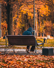 Man Sitting On A Bench Surrounded By Autumnal Leaves In A Park
