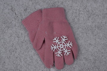 Soft pink gloves with large white snowflake on fresh snow. 