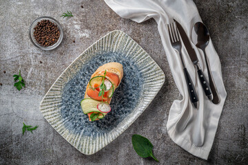 Sticker - Open sandwich with salmon, seabass, cucumber and radish on a gray stone table