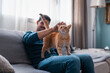 © magui RF - young man sitting on a gray sofa caresses the head of a brown tabby cat