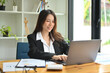 © saltdium - Photo of a beautiful insurance agent typing on a computer laptop at the wooden working desk surrounded by a document and office equipment.