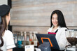 © thanmano - Beautiful caucasian waitress, a small company owner, a barista, and a bartender in a black apron standing and using cash register at the bar counter in a cafe shop