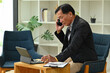 © saltdium - Photo of an elderly businessman talking on mobile phone while using a digital tablet and stylus pen at the comfortable chair.