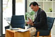 © saltdium - Photo of an elderly businessman looking on a smartphone while sitting at the comfortable chair in the modern office.