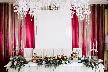 Winter Wedding decor. Winter green garland on a table with white plates and and candles. Table decorations. White candles and flowers. Setting at winter wedding reception, floral composition.