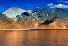 Reflection Of Mountains On Pangong Tso-Lake With Blue Sky In Background. It Is Huge Lake In Ladakh, It Is 134 Km Long And Extends From India To Tibet. Leh, Ladakh, Jammu And Kashmir, India