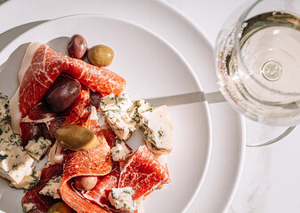 Poster - cool white wine in a glass near a plate with sliced jamon, dove cheese and various olives. a light snack on a hot day. classic italian food.