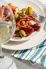 Wall Mural - cool white wine in a glass near a plate with sliced ham, dove cheese and various olives