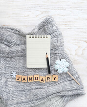 Knitted Sweater, Letter "january",  Notepad, Pencil, Snowflake Candy On White Wooden Background. January Month Calendar Concept. Winter Season. Flat Lay. Copy Space