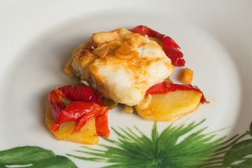 Roasted white fish with garlic red pepper and baked potato on a white plate decorated with green abstract shapes. Elegant and healthy cuisine.