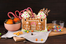 Board With Beautiful Gingerbread House And Treats On Black Wooden Background