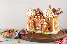 Wooden Board With Beautiful Gingerbread House And Treats On Table