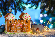 Gingerbread House, Snow, Christmas Lights And Decor On Table Against Blurred Background