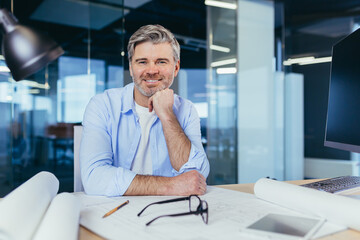 Wall Mural - Experienced gray-haired designer architect, smiling and looking at camera, man working on architectural projector of new office center