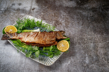 Wall Mural - Roasted Whole Trout with lemon, lettuce and dill and parsley greens on a plate against a gray stone table