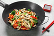 Stir fried noodles with mushrooms, chicken and vegetables in wok on light grey table