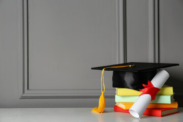Wall Mural - Graduation hat, books and diploma on white table near grey wall, space for text