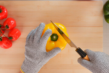 Wall Mural - Top view of a human cutting a yellow fresh pepper with gloves on a wooden board