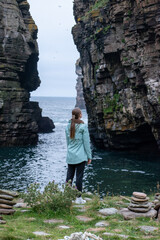 Poster - Scenic shot of a woman from her back standing on the shore of the sea looking at stone hills