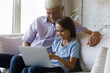 © fizkes - Happy small adorable preteen schoolboy using computer apps with joyful caring middle aged mature retired grandfather, sitting on couch at home, playing online games, shopping in internet store.