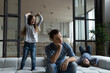 Tired thoughtful father sitting on couch while noisy daughter and son jumping in living room at home, unhappy depressed young man dad or babysitter feeling exhausted by naughty active children