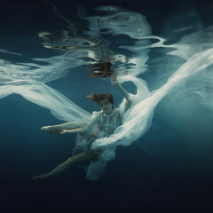 Wall Mural - A girl in a white dress posing underwater on a dark background as if she were in zero gravity