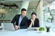 © saltdium - Photo of young office workers sitting together at the working desk surrounded by a computer laptop, digital tablet and office equipment.