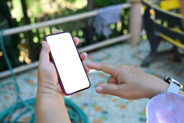 Poster - Photo of elder lady hand holding a white blank screen smartphone over the sunny balcony as background.