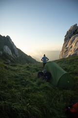 Wall Mural - Tranquil scenery of a hiker outside the tent admiring the sunrise on top of the mountain