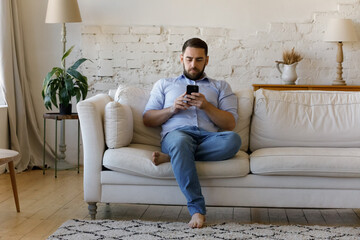 concentrated young man using cellphone software applications, reading news, typing message sending e