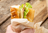 Fototapeta Tulipany - A man holds in his hand a sandwich with meat and cheese. Sandwich cubano, traditional fast food.