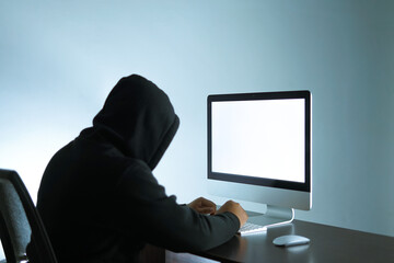 unidentified man wearing a black hoodie is sitting in front of the white blank screen. a portrait that is suitable for background campaign of the internet threats.