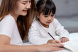 © FAMILY STOCK - Beautiful Asian woman helping her daughter with homework at home.